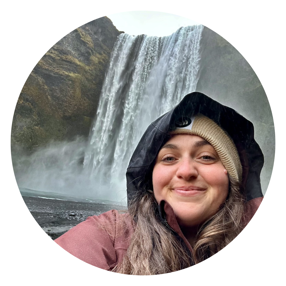 Woman in a rain coat taking a selfie in front of a waterfall.