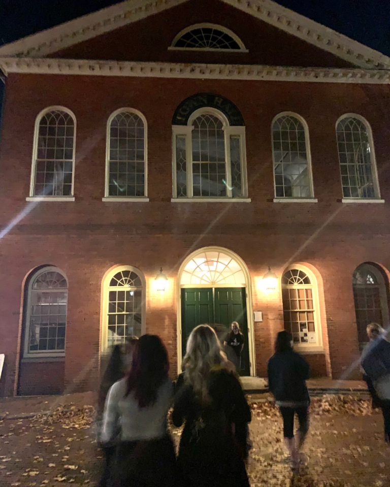Woman giving tour in front of the Salem Old Town Hall at night.
